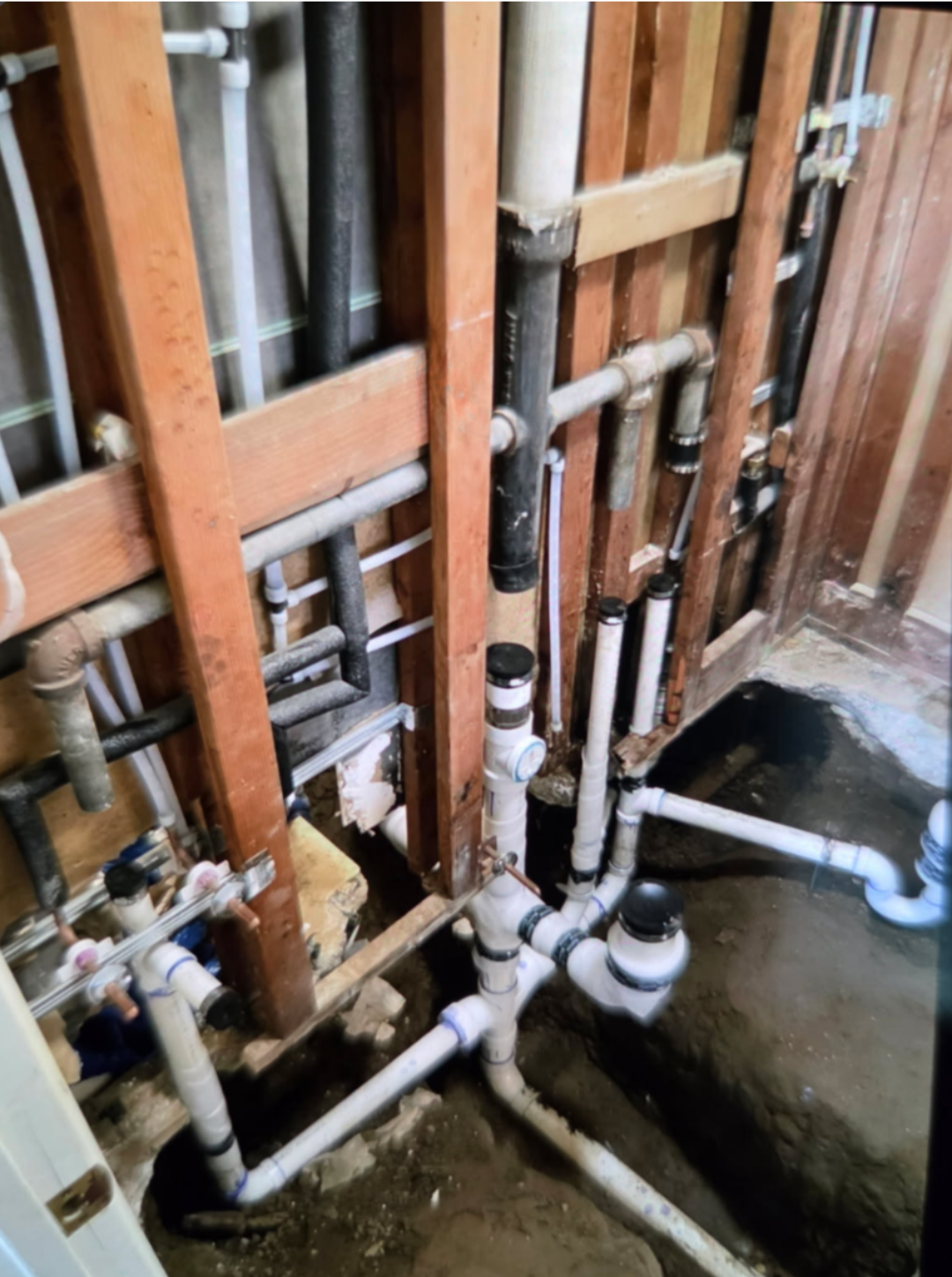 Open wall framing with new drain, vent and supply piping installed during a plumbing rough-in.