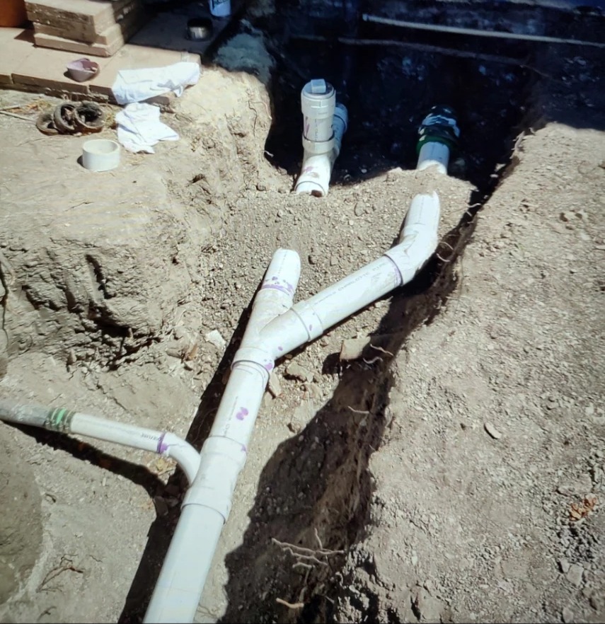 Open trench with newly installed PVC sewer line, wye fitting and cleanout risers before backfill.