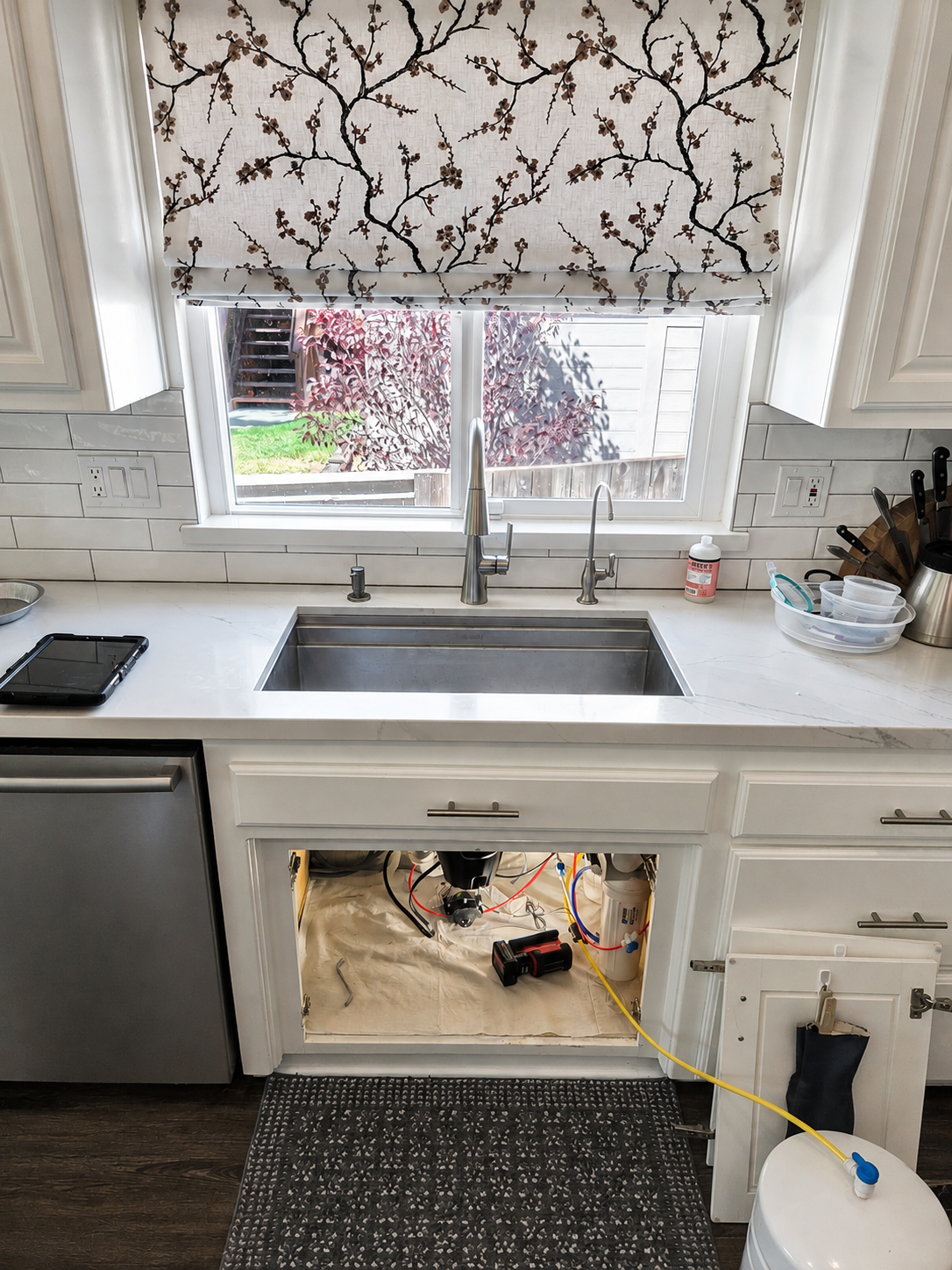 Kitchen sink with a newly installed pull-down faucet and filtered-water dispenser, with the cabinet below open showing the new supply lines and filtration during installation.
