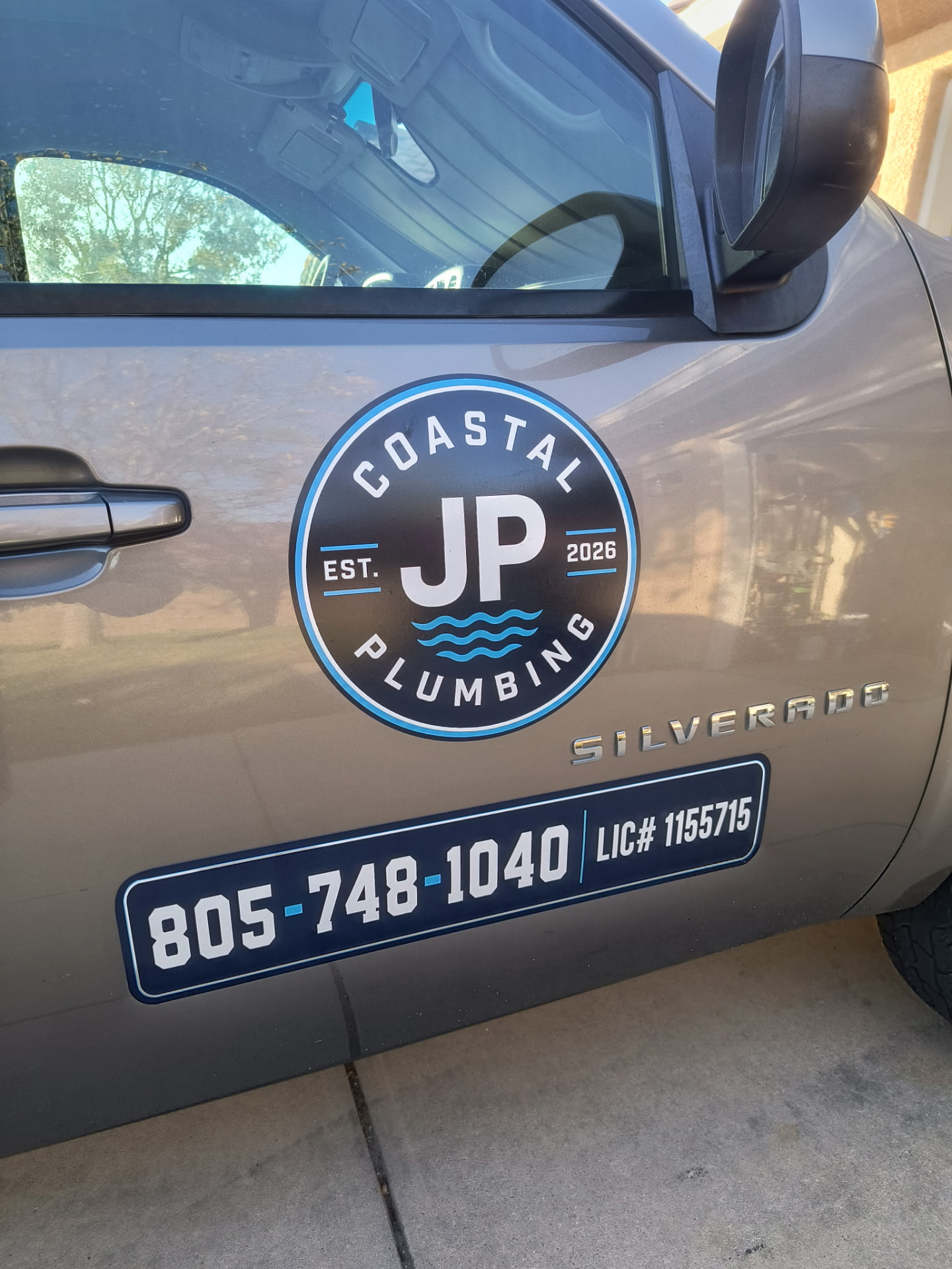 Close-up of the JP Coastal Plumbing door decal showing the company logo, phone number and contractor license number.