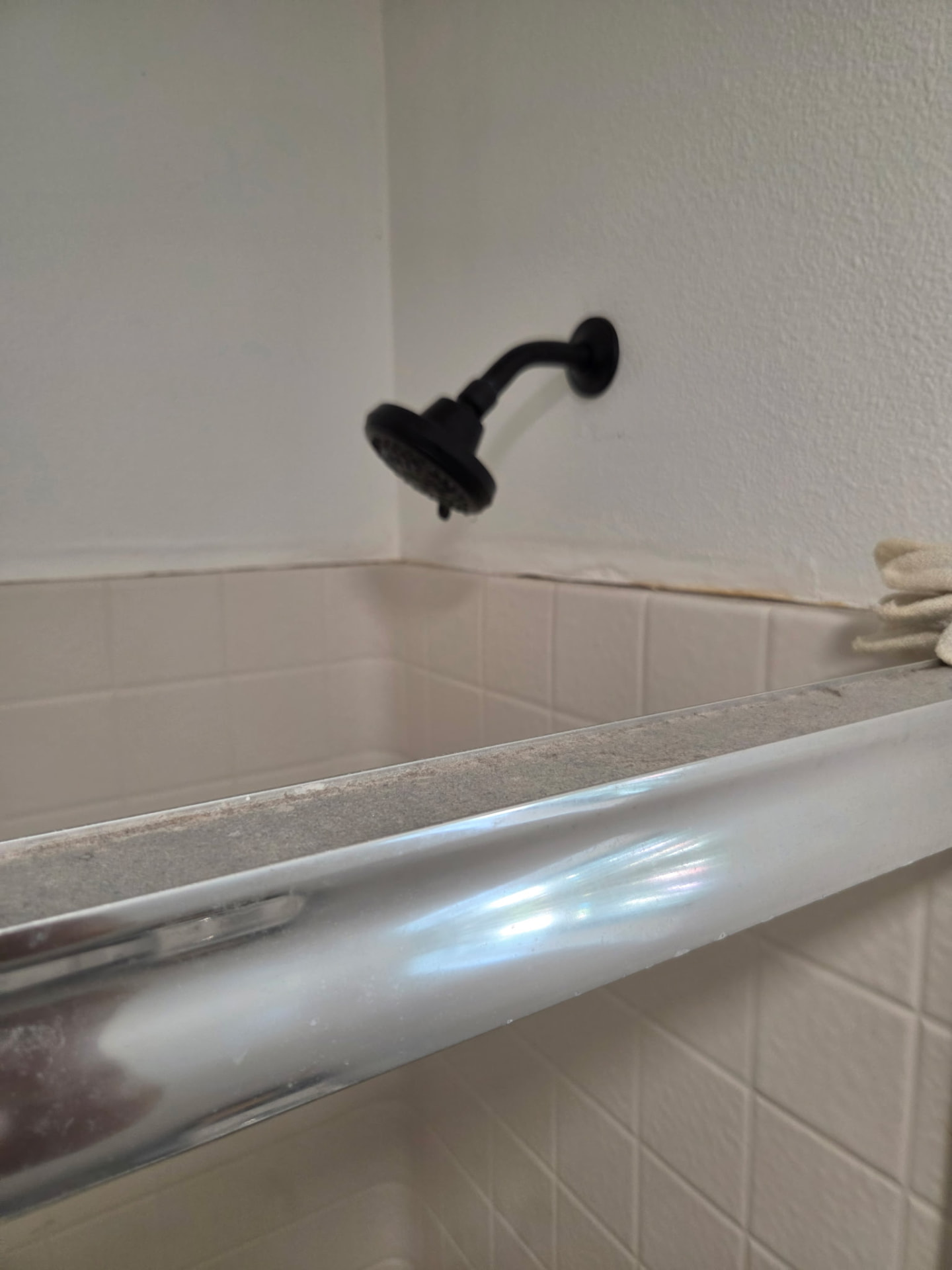 Newly installed matte black shower head and arm on a tiled tub surround.