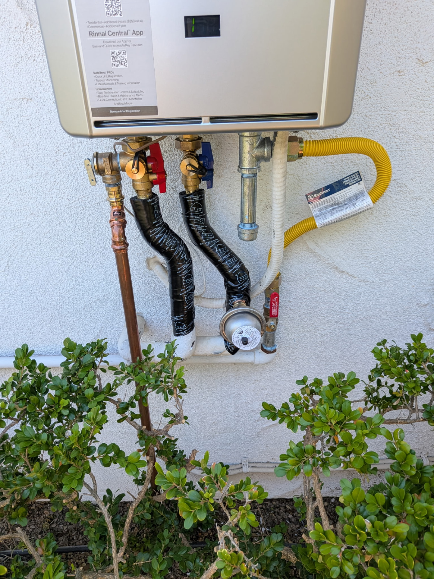 Close-up of the service valves, gas connector, expansion tank and insulated copper lines beneath a Rinnai tankless water heater.