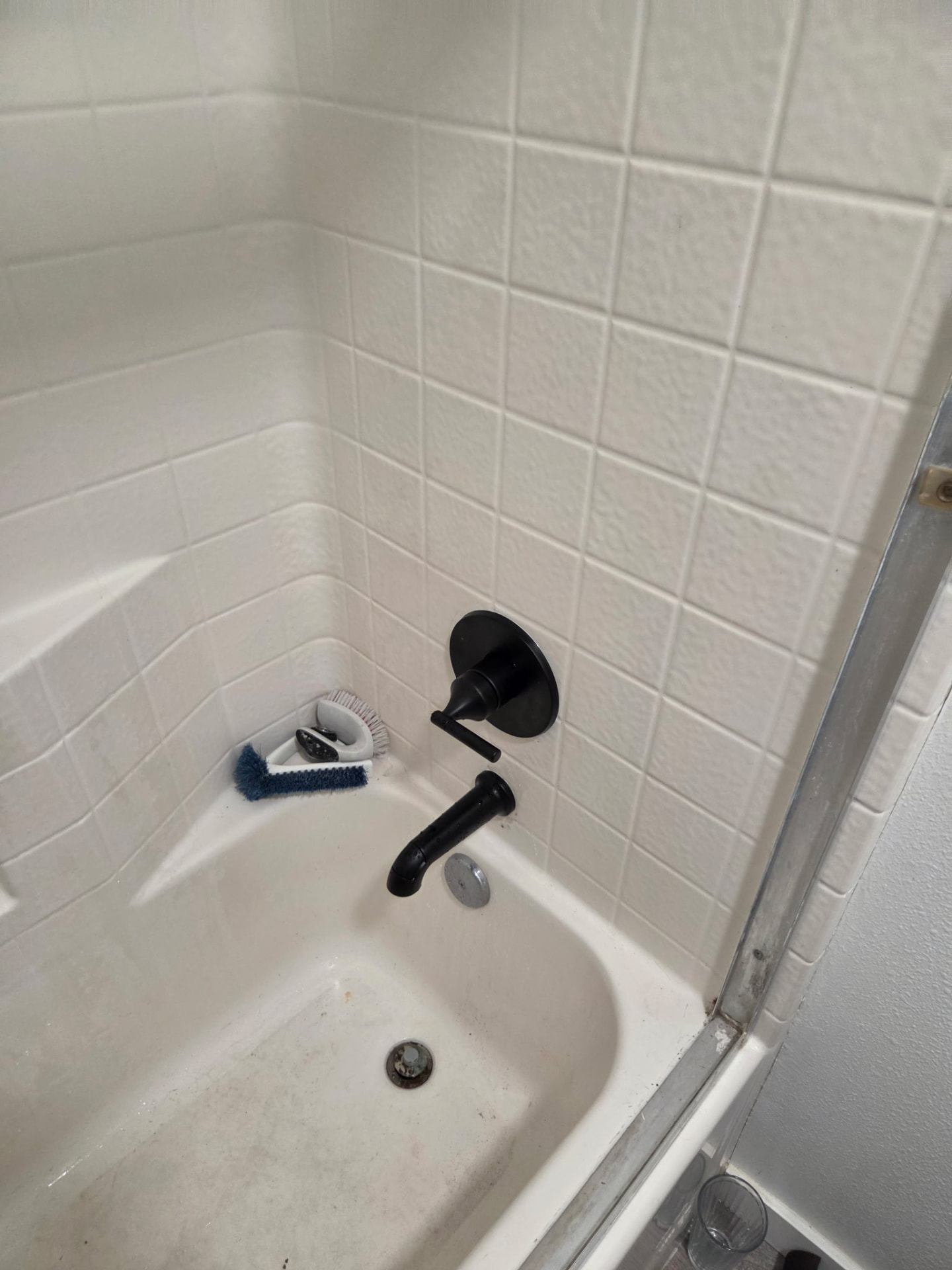 Matte black tub spout and single-handle shower valve trim installed in a white tiled bathtub alcove.