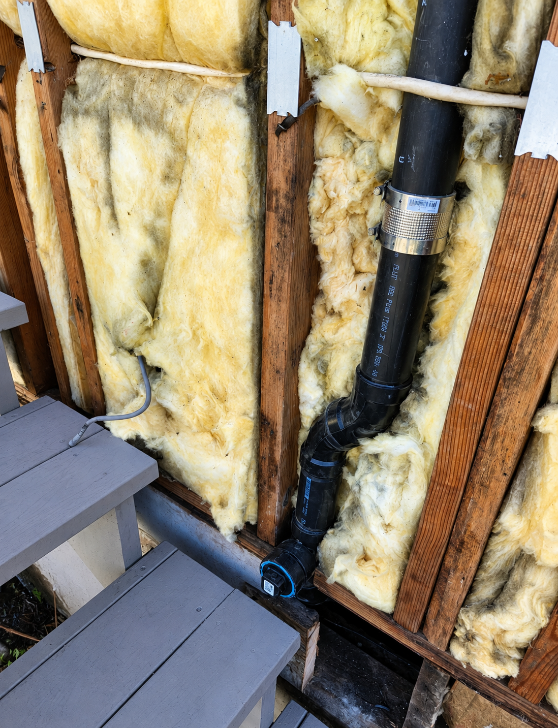 New ABS drain and vent piping installed in an open exterior wall cavity with a shielded coupling and cleanout.