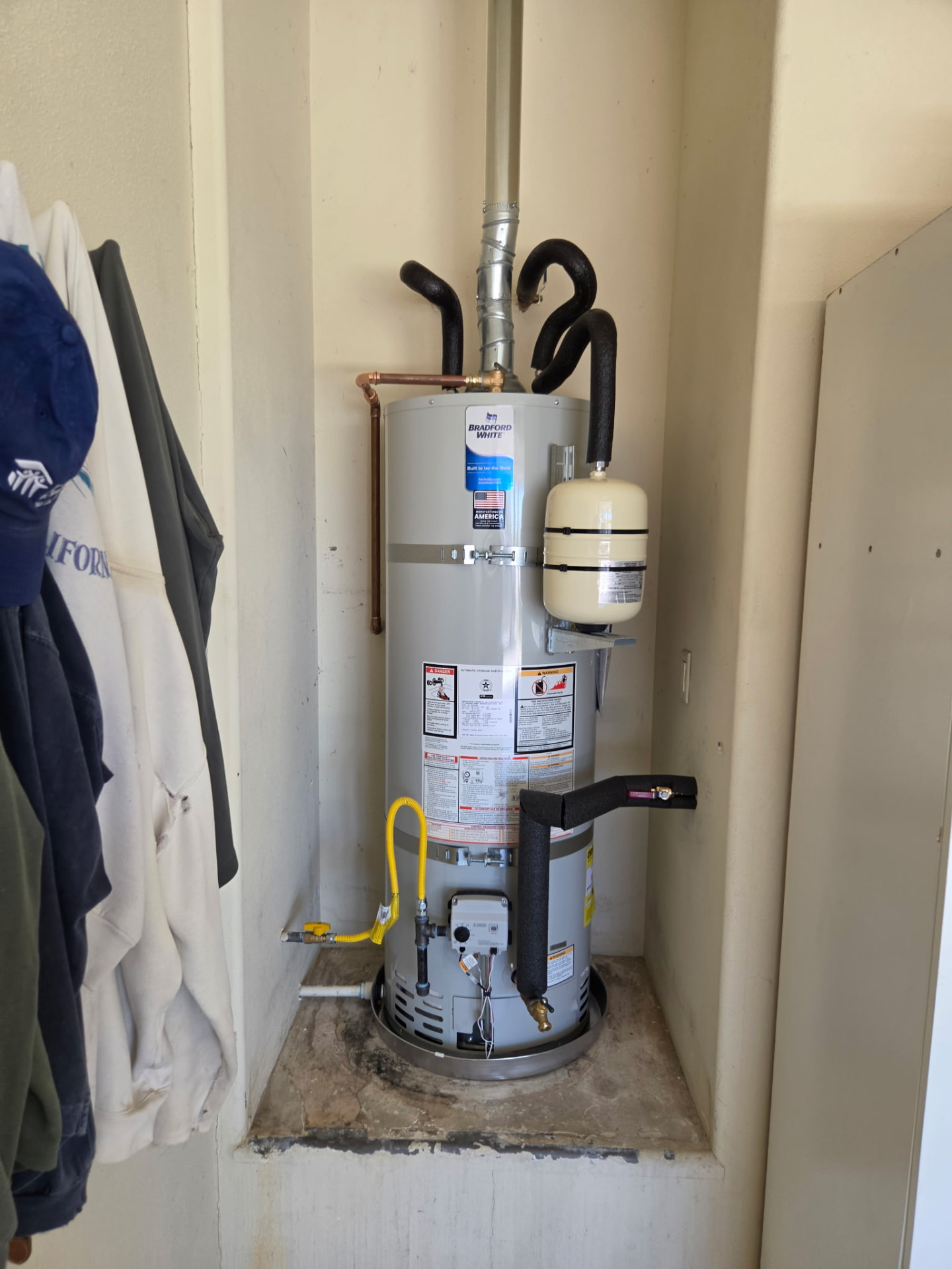 Bradford White gas water heater with expansion tank and insulated lines installed in a utility closet.