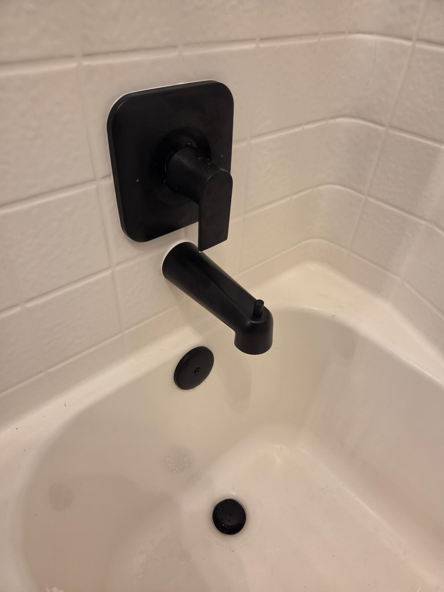 Matte black tub spout and single-handle shower valve trim installed in a white tiled bathtub surround.