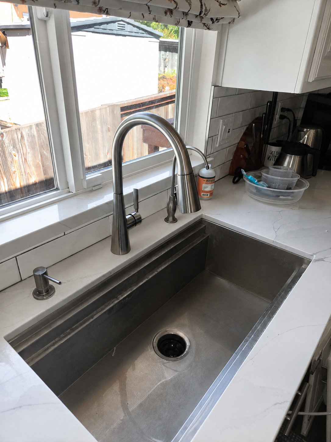Close-up of a brushed nickel pull-down kitchen faucet, soap dispenser and stainless steel sink after installation.